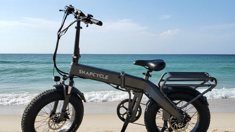 Snapcycle e-bike on a real sandy ocean beach with gentle turquoise waves and blue sky