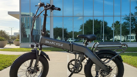 Snapcycle e-bike on a sunny city bike path beside a modern glass building